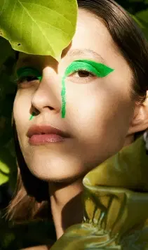 A person with green make-up stood amongst leaves.